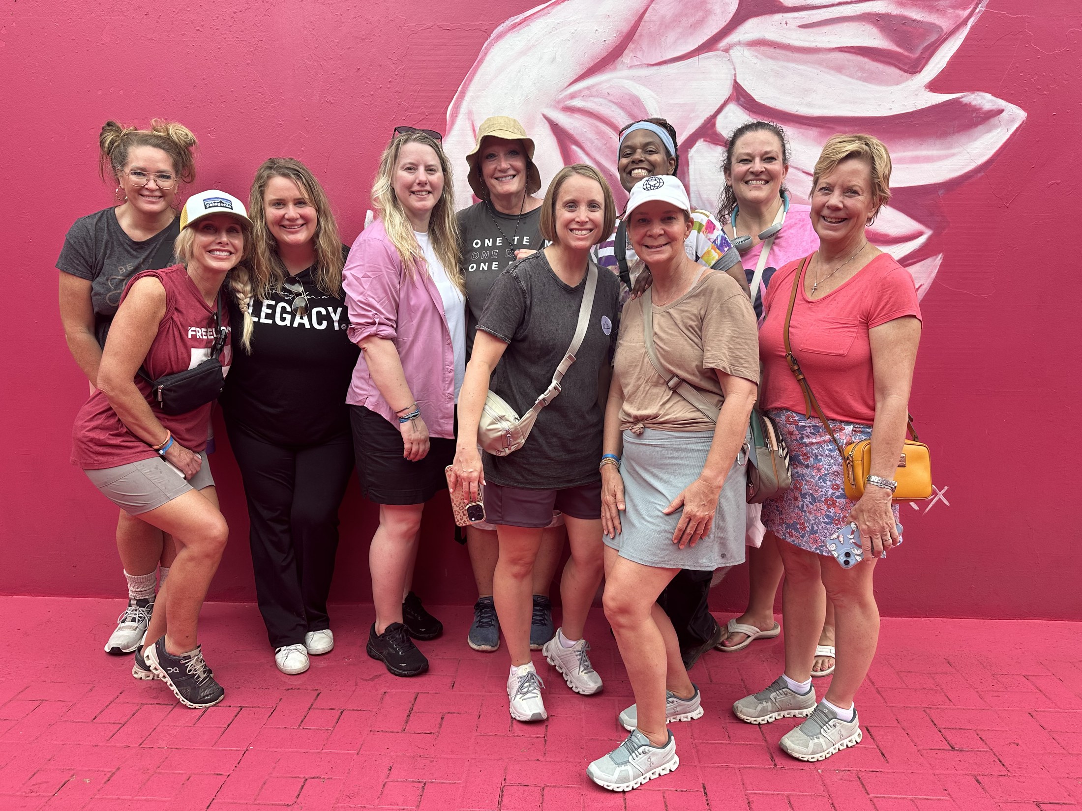 Women gather in front of a colorful pink mural during a community visit.