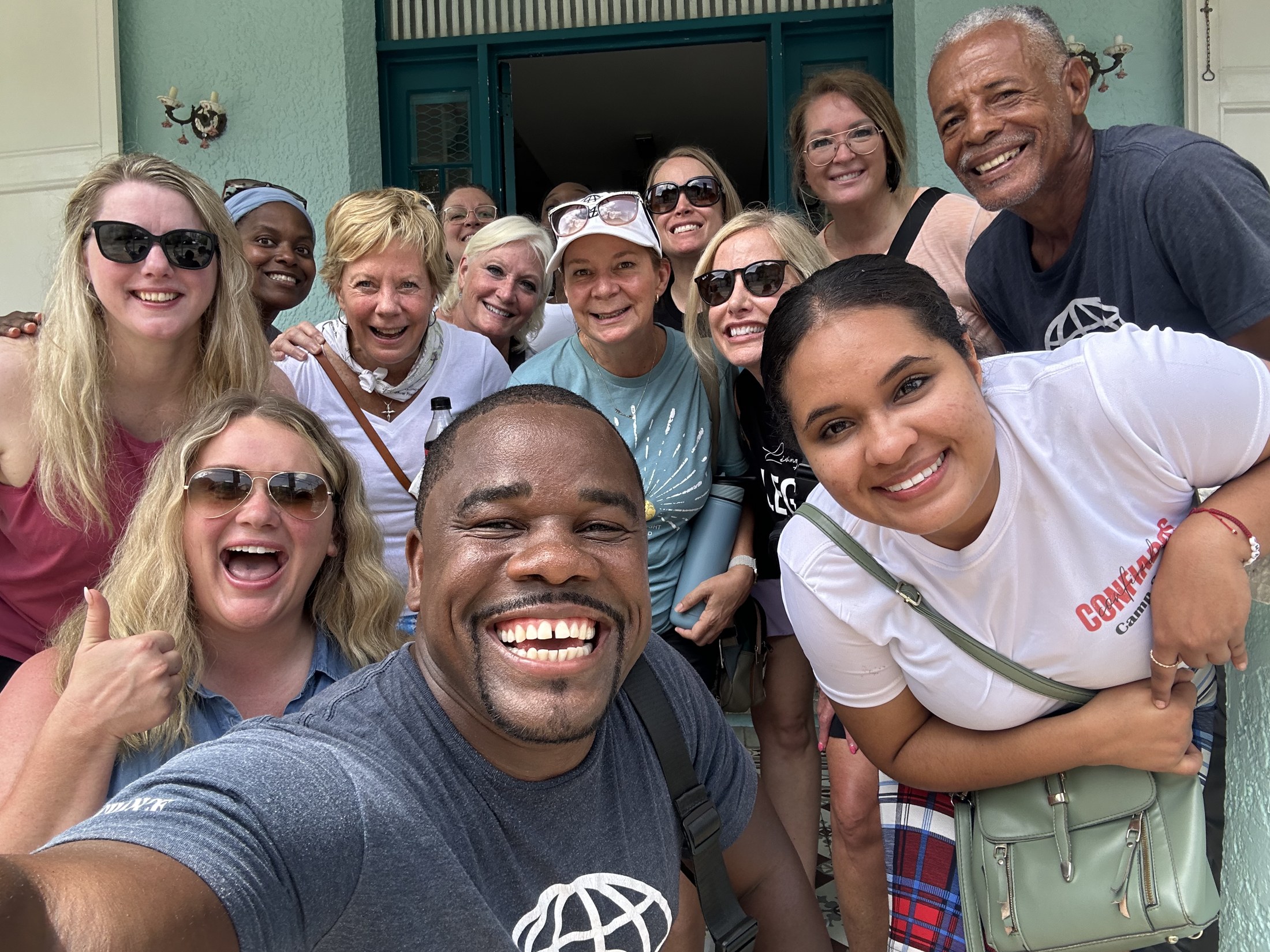 A smiling group gathers with community members during a visit.
